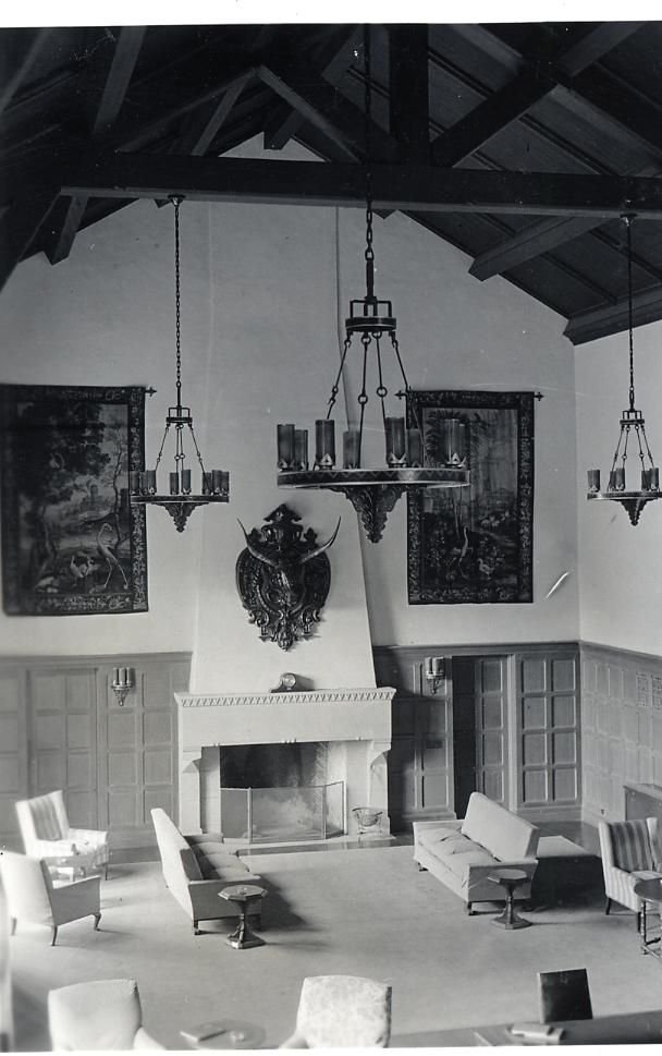 Dabney Lounge in an early photograph: a high beamed ceiling, iron chandeliers, tapestries, and a stone fireplace.